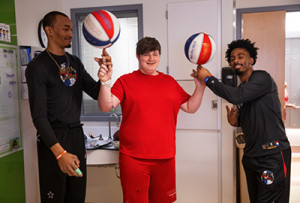 Hoops Family Children’s Hospital patient Ashton Maynard, age 17, spins two basketballs with the assistance of Harlem Globetrotters, “Crash” and “Too Tall,” during their visit to the children’s hospital on Wednesday, March 27, 2024.